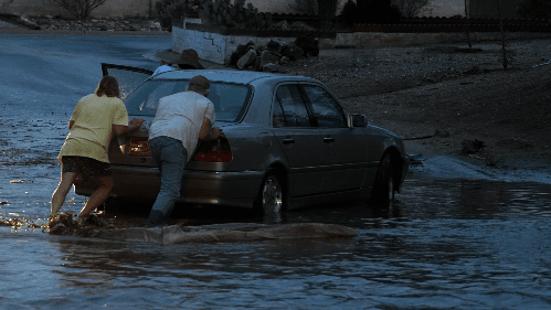 Residents push a stalled sedan through thigh‑deep floodwater after a monsoon storm inundated Tucson streets on July 11, 2026.