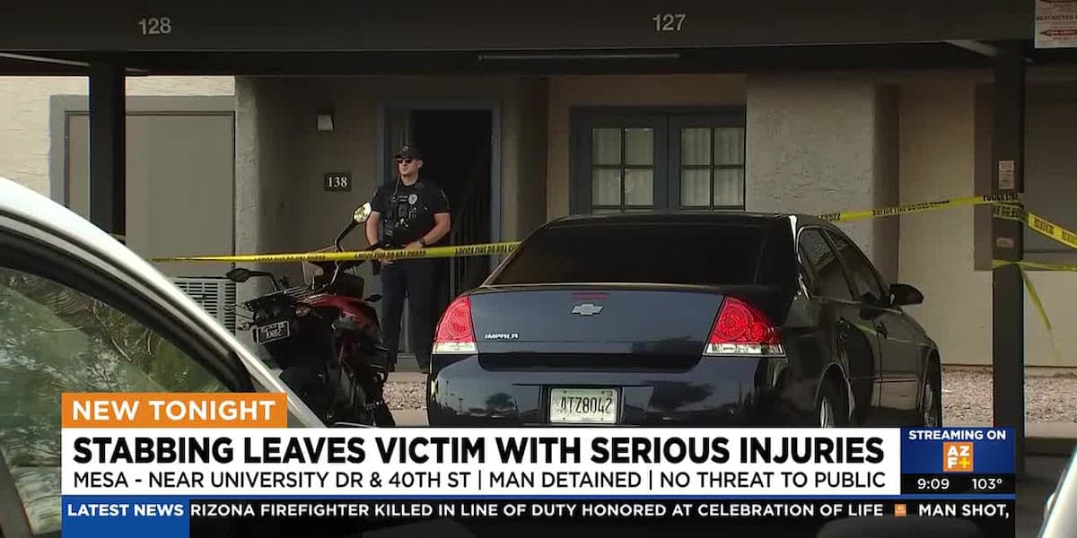 Police tape and an officer at the entrance of an apartment carport in Mesa after a reported stabbing that left a victim seriously injured, shown in a news broadcast still.