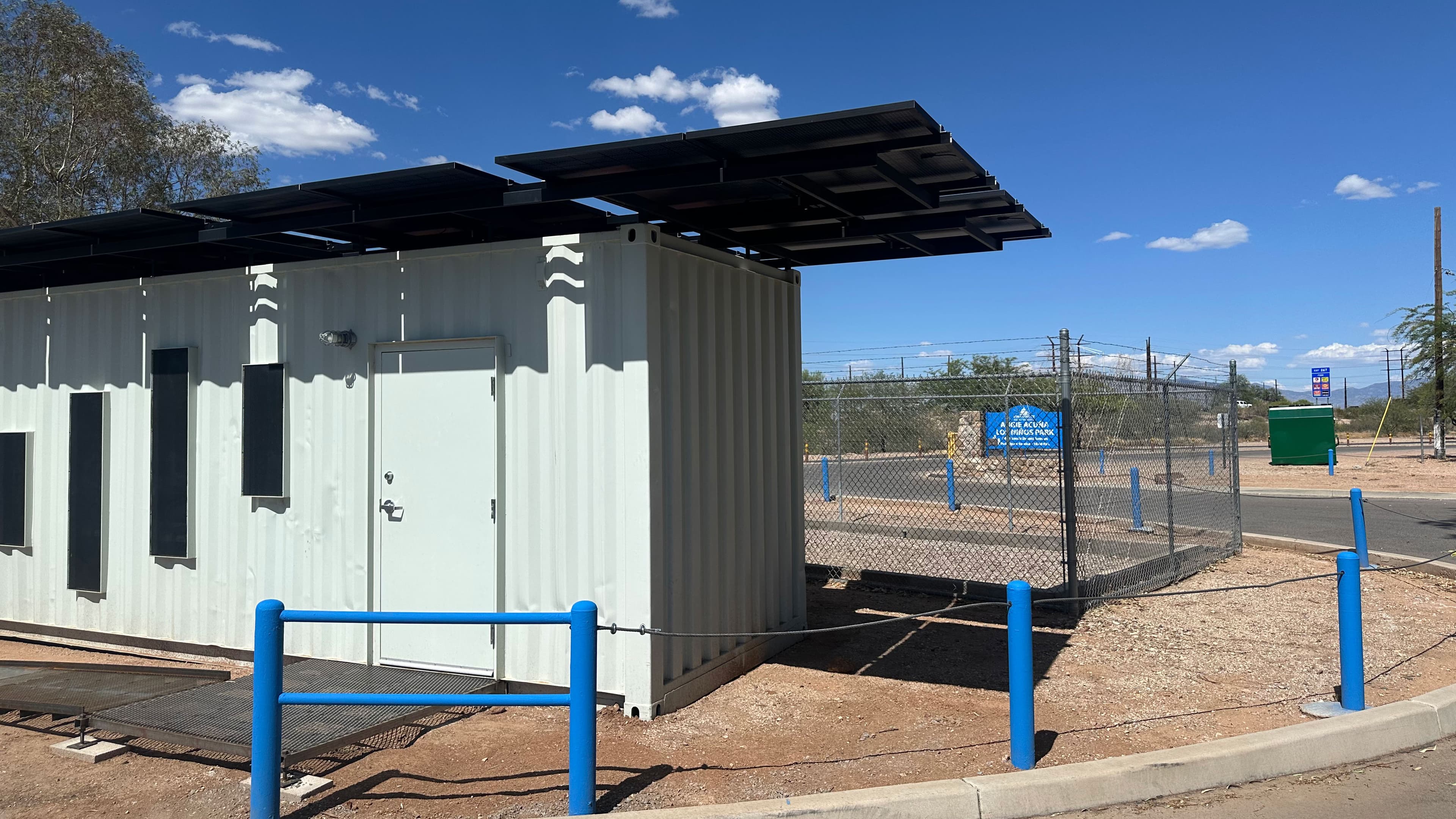 The newly opened COOLTainer on Tucson’s South Side, showing the white container, solar-panel canopy and the fenced site near a neighborhood street.