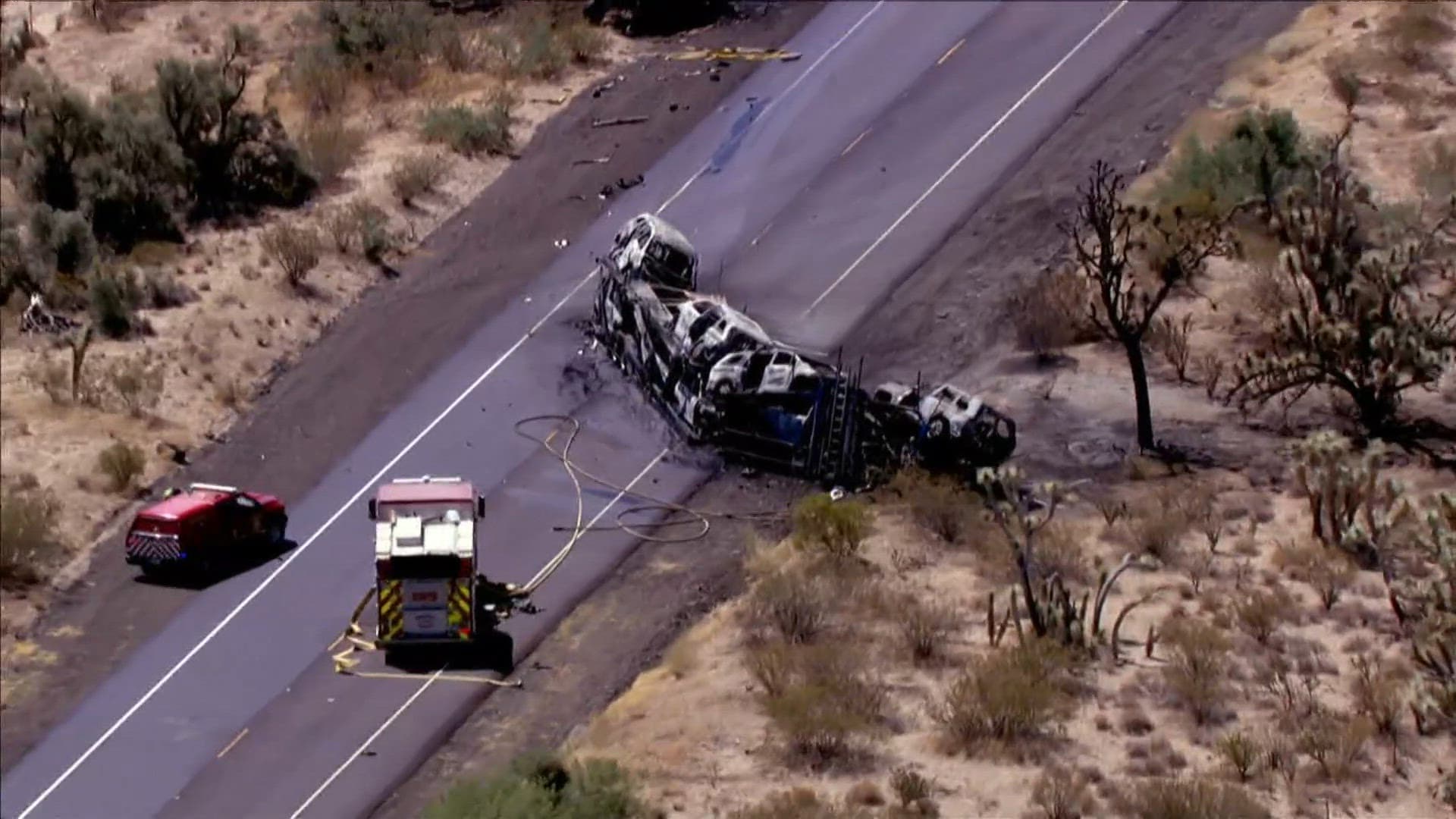 Aerial view of a charred car carrier and emergency vehicles on a rural highway — scenes like this can force temporary closures and disrupt weekend travel.
