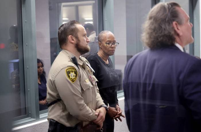 A woman in custody appears in court, flanked by law enforcement and attorneys, after an arrest related to the fatal Mesa collision, officials say.
