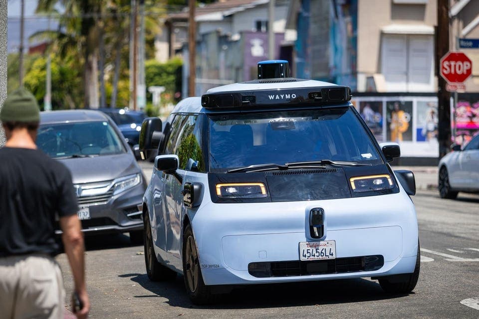 A Waymo autonomous minivan driving on a public street in California; Waymo is importing thousands of such self‑driving vehicles into the U.S. fleet.