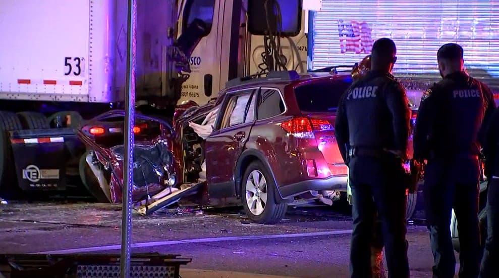 West Phoenix — A heavily damaged SUV is shown next to a semitruck trailer as police stand at the crash scene on Buckeye Road, where a deadly collision closed the roadway.