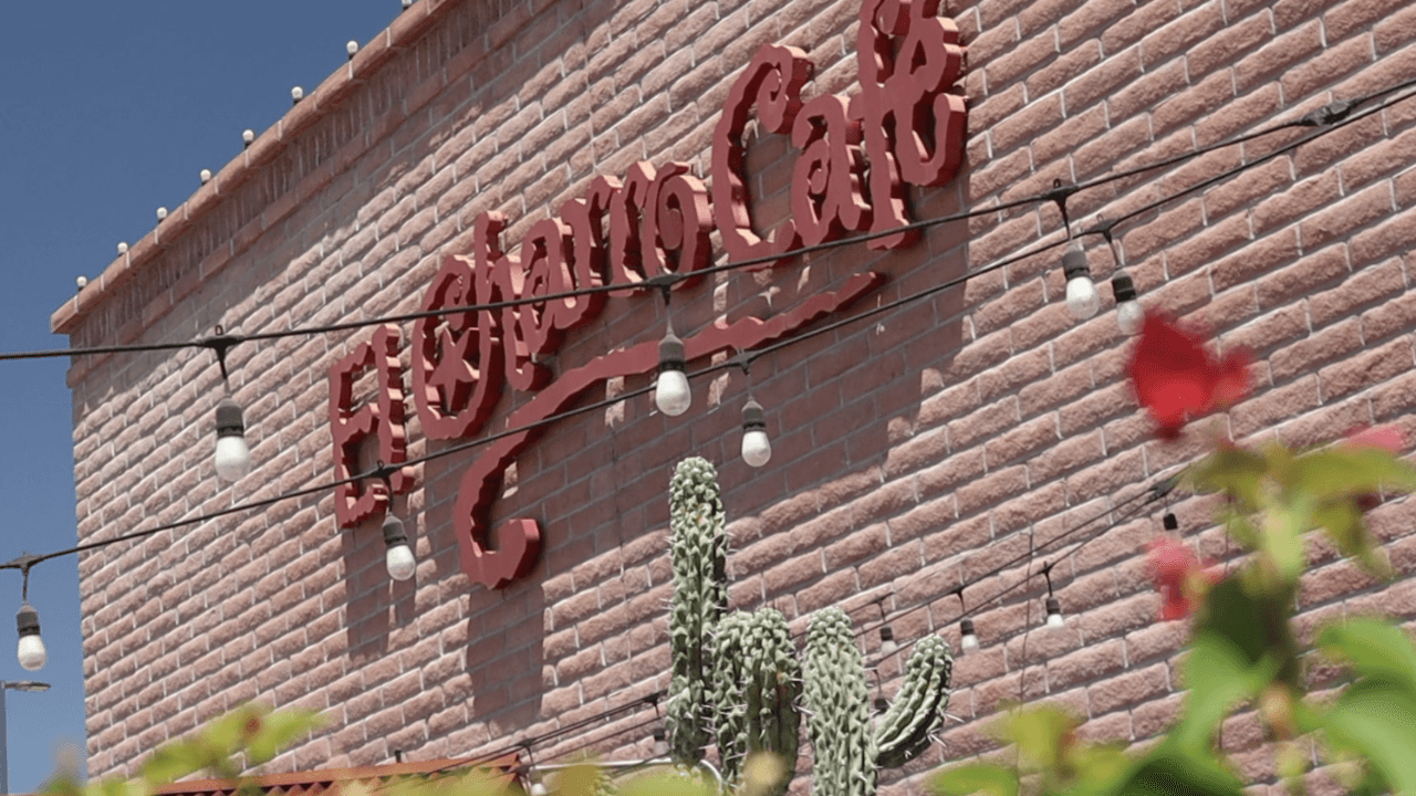 El Charro Café sign mounted on a brick wall with string lights and cactus in the foreground at the historic Tucson restaurant.