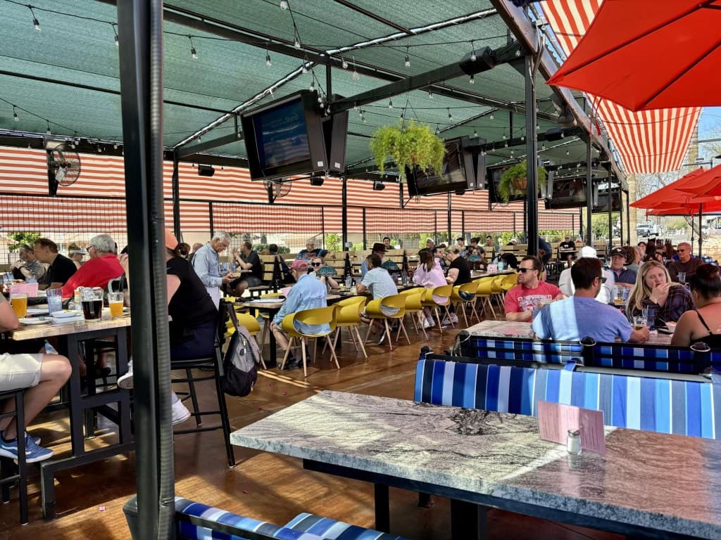 A busy, shaded outdoor patio with multiple TVs and patrons watching a match — representative of the lively bars and restaurants recommended for cheering on the U.S. in the World Cup.