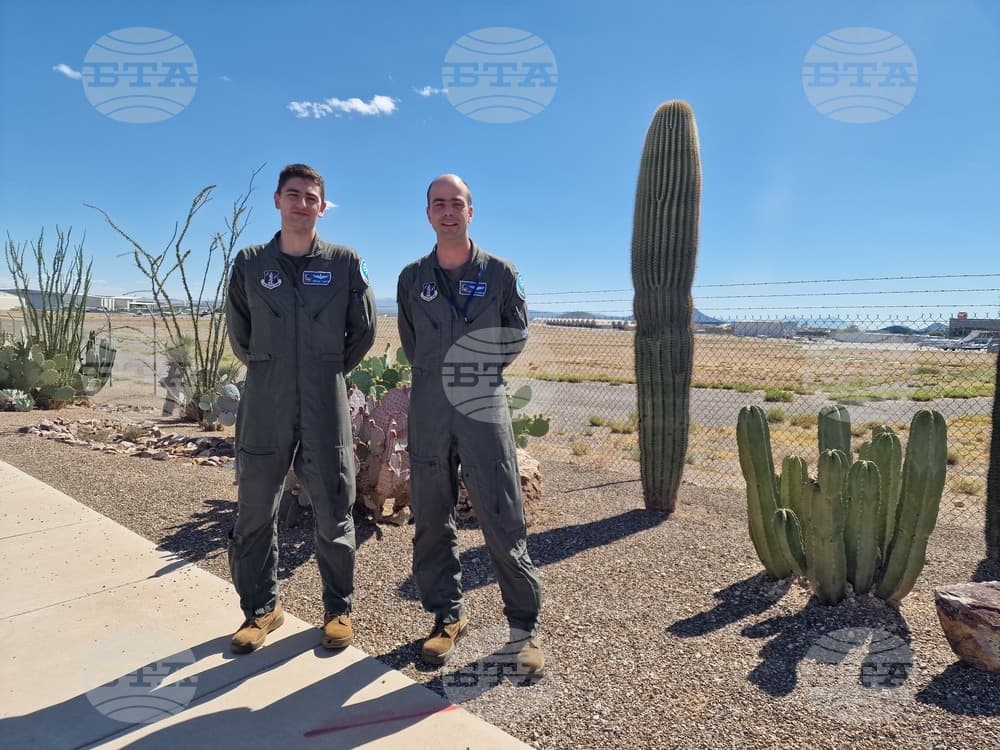 Two Bulgarian F-16 pilots in flight suits stand by cacti at a Tucson, Arizona training base during F-16 training, illustrating the hot, arid conditions they cited as a major challenge (BTA Photo/Irina Shopova)