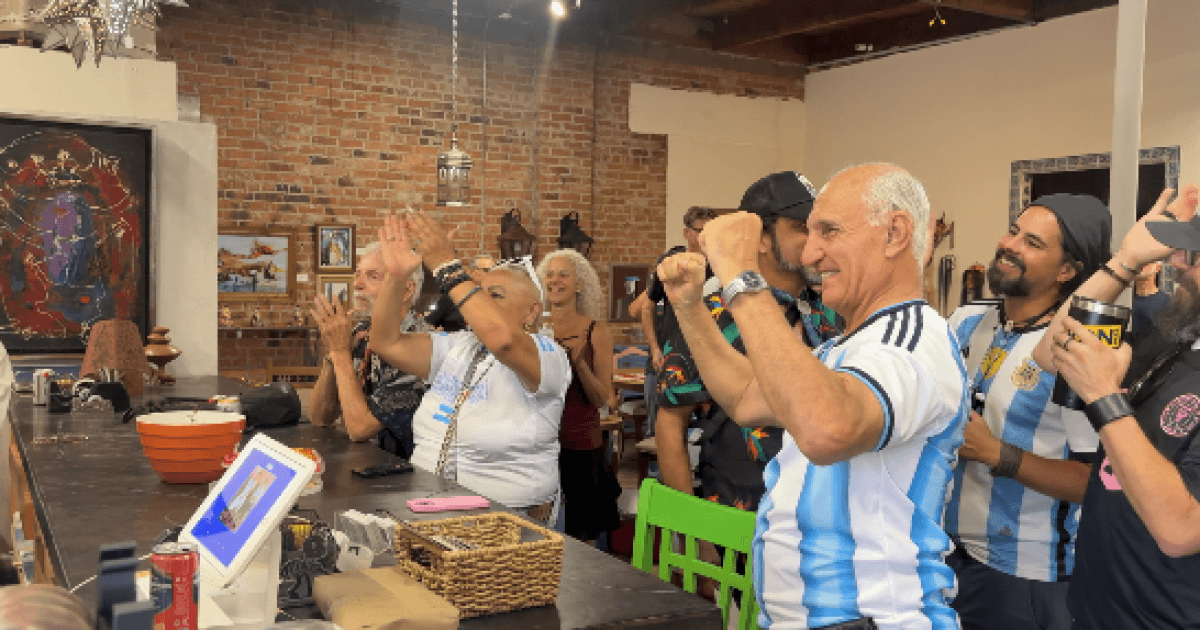 Fans at the Lost Barrio Gallery in Tucson cheer and celebrate during a World Cup watch party, many wearing Argentina jerseys.