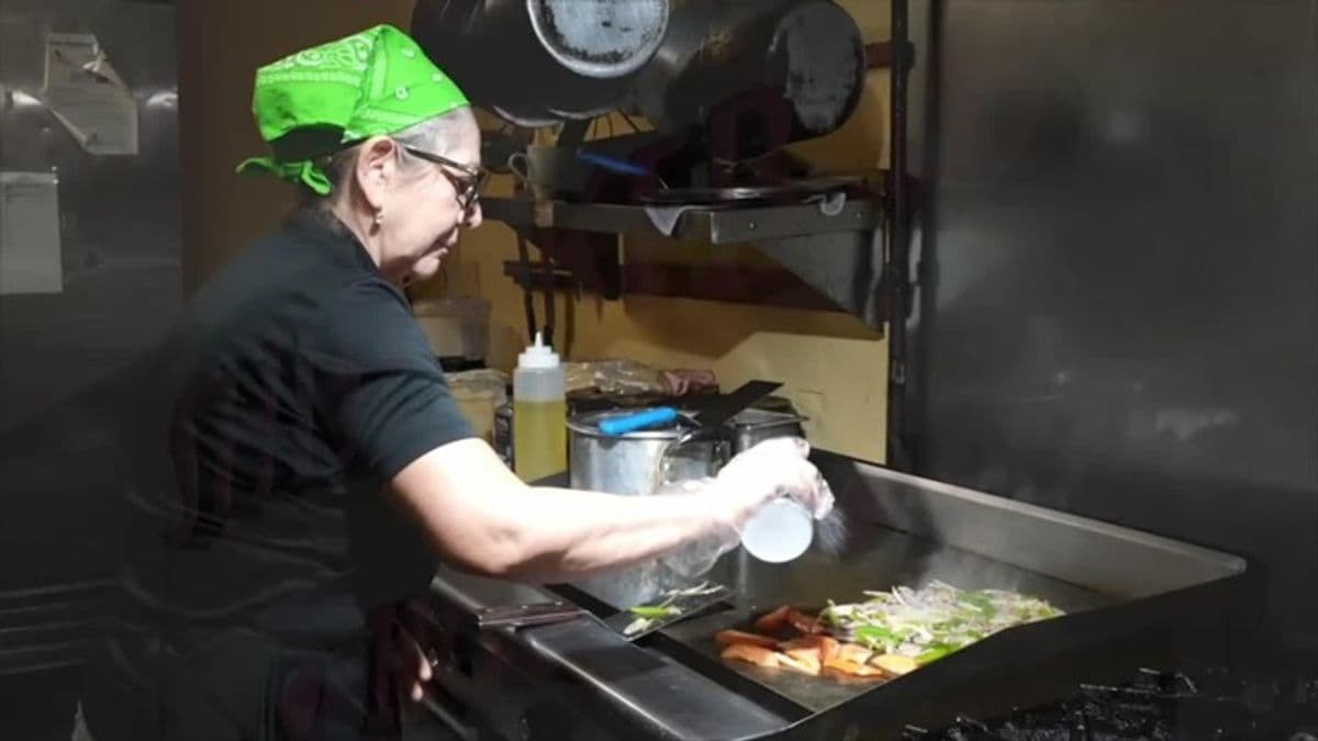 A cook at Shish Kebab House seasons and sautés vegetables on a flat-top grill inside the restaurant, illustrating the hands-on preparation of produce central to the eatery's menu as it faces rising wholesale costs.