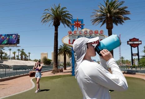 A visitor drinks water and shields from the sun near the 'Welcome to Fabulous Las Vegas' sign as Las Vegas swelters during the heatwave.