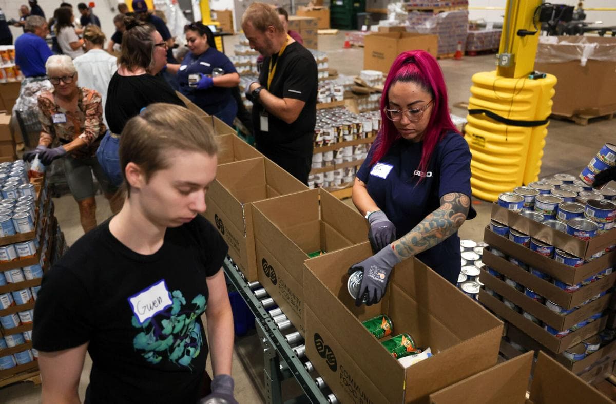 Volunteers pack canned goods into boxes at the Community Food Bank of Southern Arizona warehouse in Tucson, preparing food boxes for families facing increased summer food insecurity.