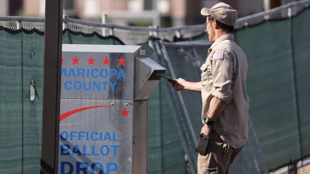A voter drops a ballot into an official Maricopa County ballot drop box at the Maricopa County Tabulation and Election Center; Arizona's 2026 primary voting runs June 24–July 21.