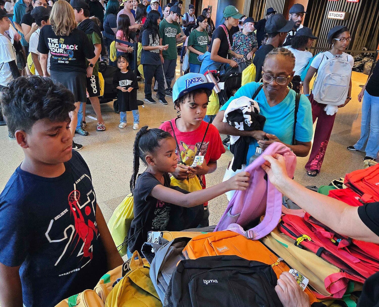 Parents and children crowd a distribution table at a Phoenix-area back-to-school giveaway, selecting backpacks and supplies.
