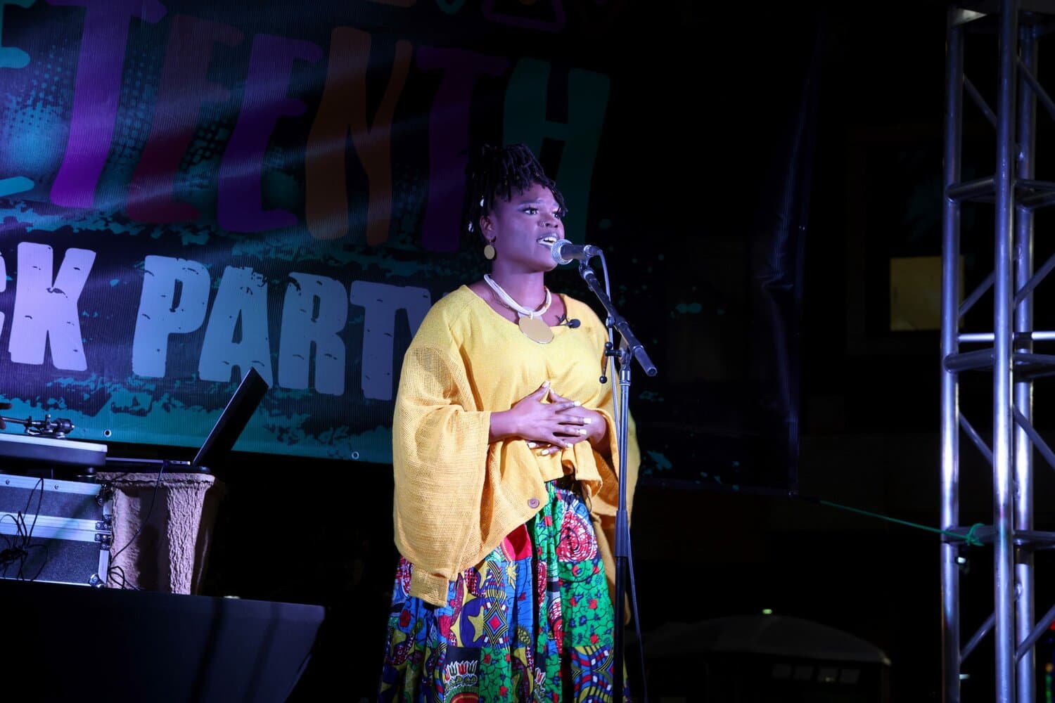 A speaker at a microphone stands in front of a large Juneteenth banner during a Tempe community event, addressing attendees about the holiday.